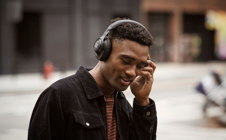 A man listening to headphones with the blurred image of a city street behind him.