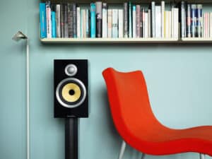 A floorstanding Bowers & Wilkins speaker next to a colorful bookshelf and red chair.