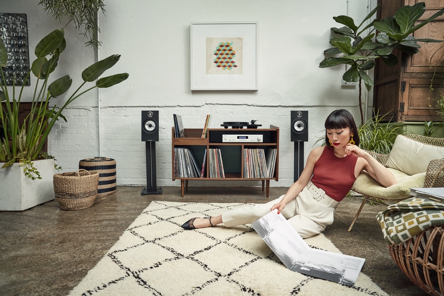 Woman sitting on the ground of a living room with a high-end audio system in the background.