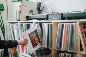 A person takes an album from a large rack holding an album collection and two turntables on top of it.
