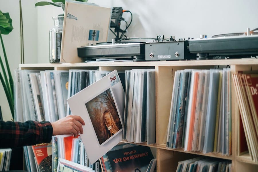 A person takes an album from a large rack holding an album collection and two turntables on top of it.
