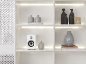 A Bowers & Wilkins bookshelf speaker in a white cabinet. Vases are in the other cabinet compartments.