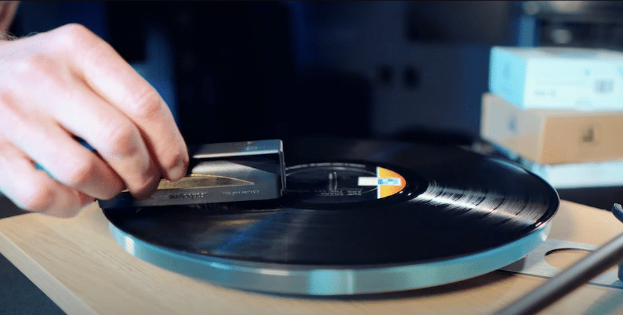 Close up of a hand holding a brush cleaning a vinyl record on a turntable. 