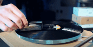 Close up of a hand holding a brush cleaning a vinyl record on a turntable.