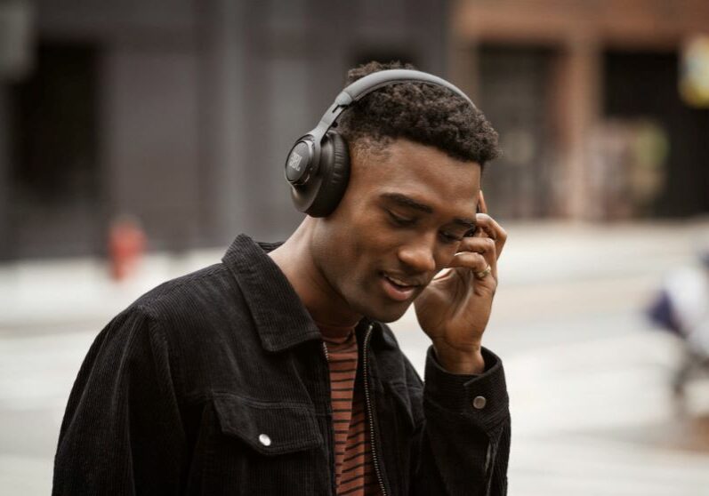 A man listening to headphones with the blurred image of a city street behind him.