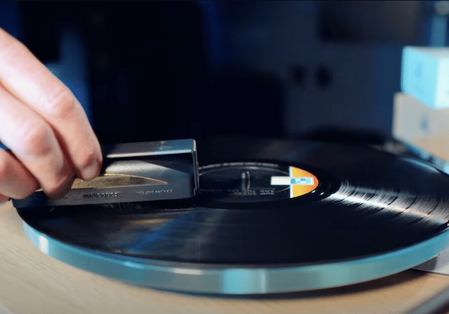 Close up of a hand holding a brush cleaning a vinyl record on a turntable.